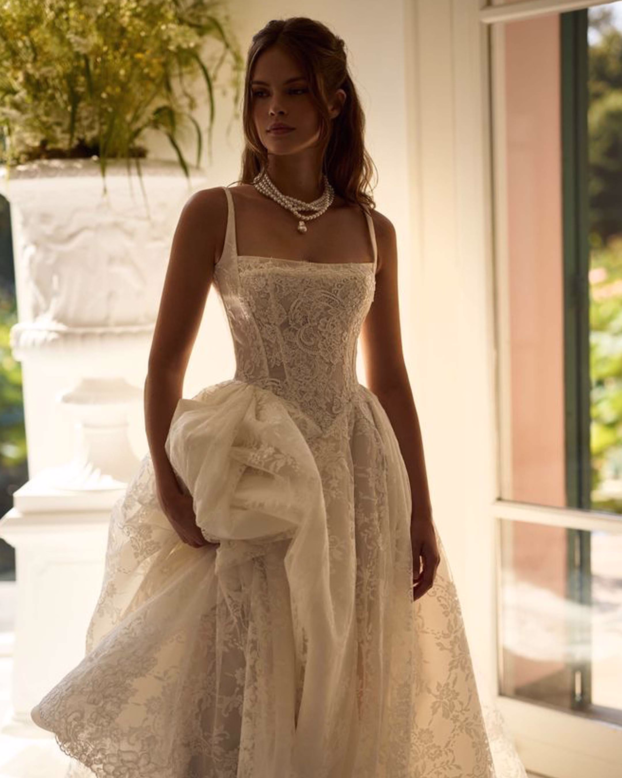 Milla Nova Melrose A-line Chantilly lace wedding dress with a Basque waist corset bodice, straight neckline, spaghetti straps, and dramatic lace train.