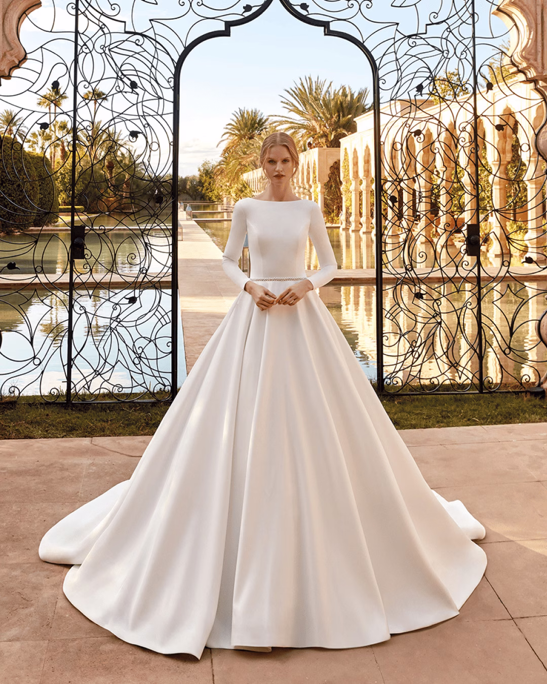 Demetrios Style 1127 satin ball gown wedding dress with a bateau neckline, long sleeves, beaded bodice, high illusion back, and cathedral-length train.