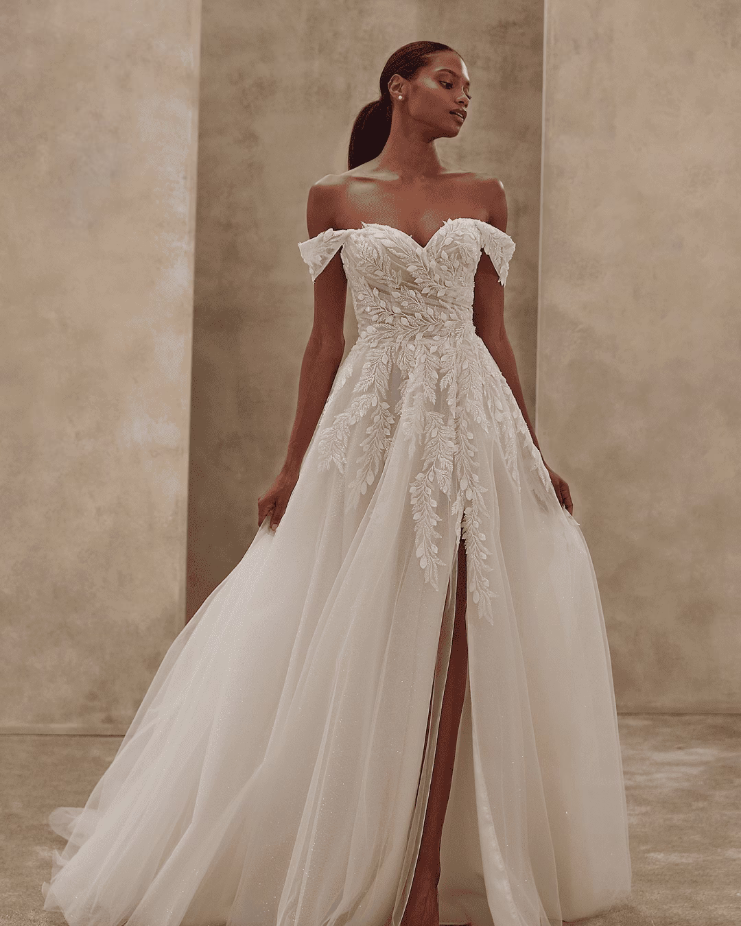 Demetrios Style 1541 A-line wedding dress with off-the-shoulder sweetheart neckline, beaded leaf lace, sparkling tulle, sculpted bodice, front slit, and flowing train.