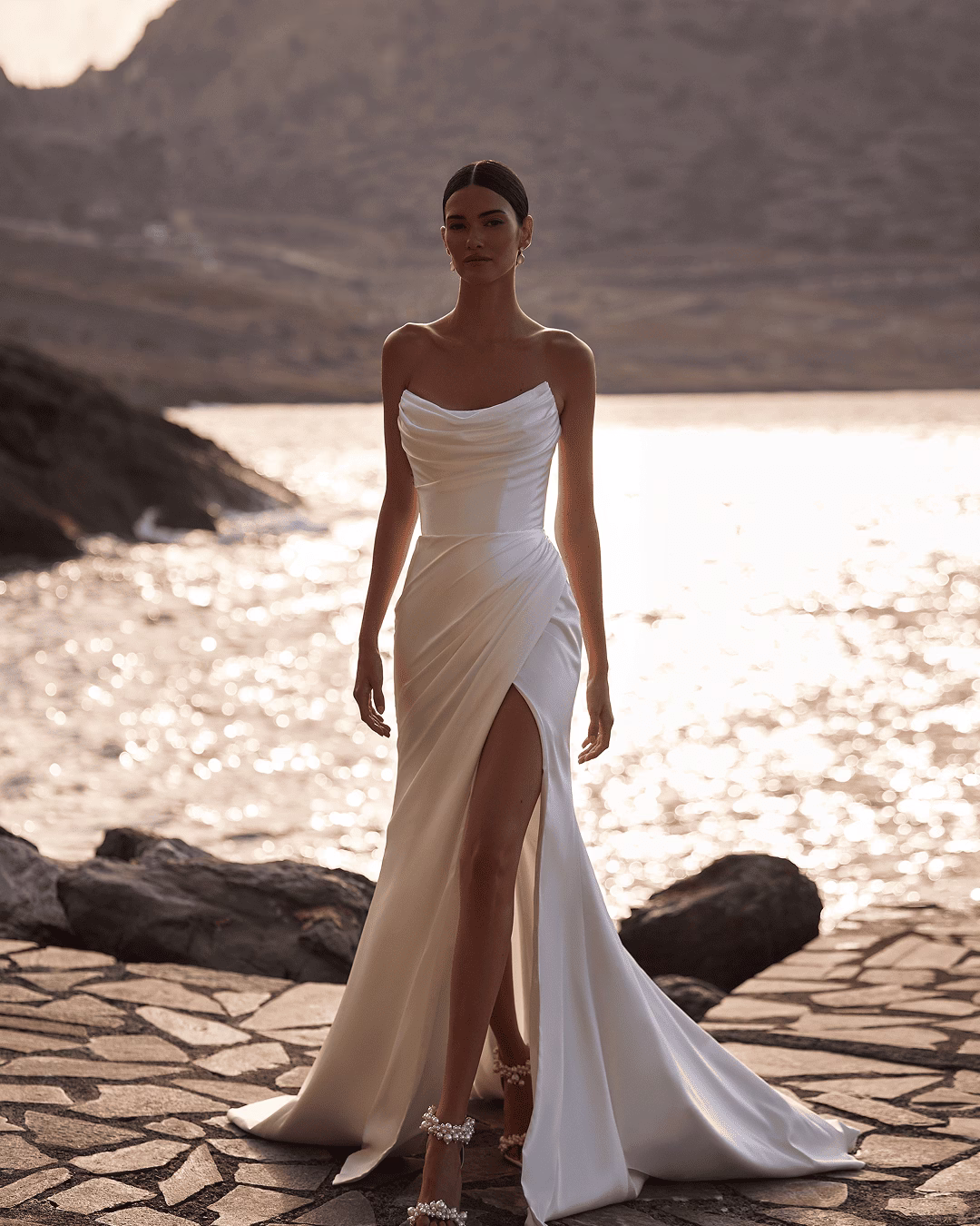 Milla Nova Bellissima satin mermaid wedding dress with a structured corset bodice, draped neckline, thigh-high slit, side draping, and subtle train.